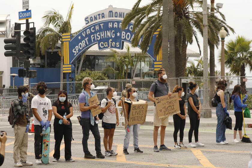 SANTA MONICA, CA - JUNE 01: A few protestors stood in the middle of Ocean Ave at Colorado where the National Guard stands at the Santa Monica Pier even as brigades of people with brooms descended on the upscale shopping district of Santa Monica Monday morning after looters spent hours yesterday smashing windows, stealing items and setting several fires. Protestors once again gathered en masse in the midst of the coronavirus outbreak to protest the death of George Floyd, an unarmed black man who died last week in police custody after a white Minneapolis police officer pinned him down by his neck for several minutes. Santa Monica on Monday, June 1, 2020 in Santa Monica, CA. (Al Seib / Los Angeles Times)