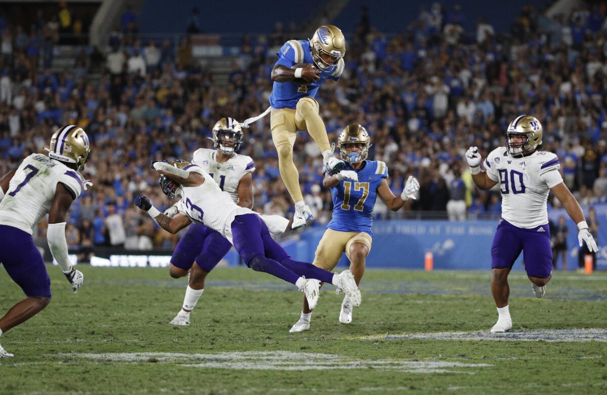 UCLA quarterback Dorian Thompson-Robinson leaps over Washington linebacker Kamren Fabiculanan for extra yards.