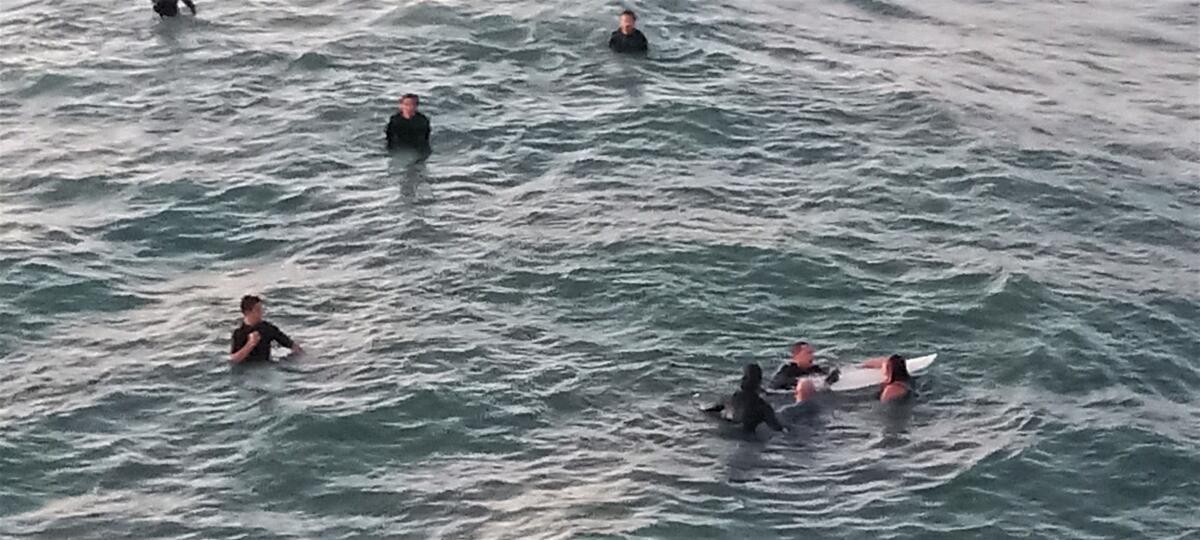 Surfers near the Huntington Beach Pier Sunday evening help a man and woman who jumped off the pier.