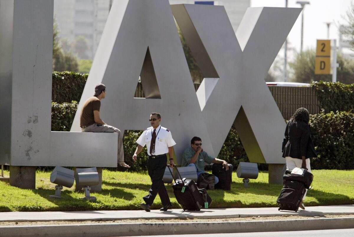 Travelers sit on the LAX Los Angeles International Airport sign.