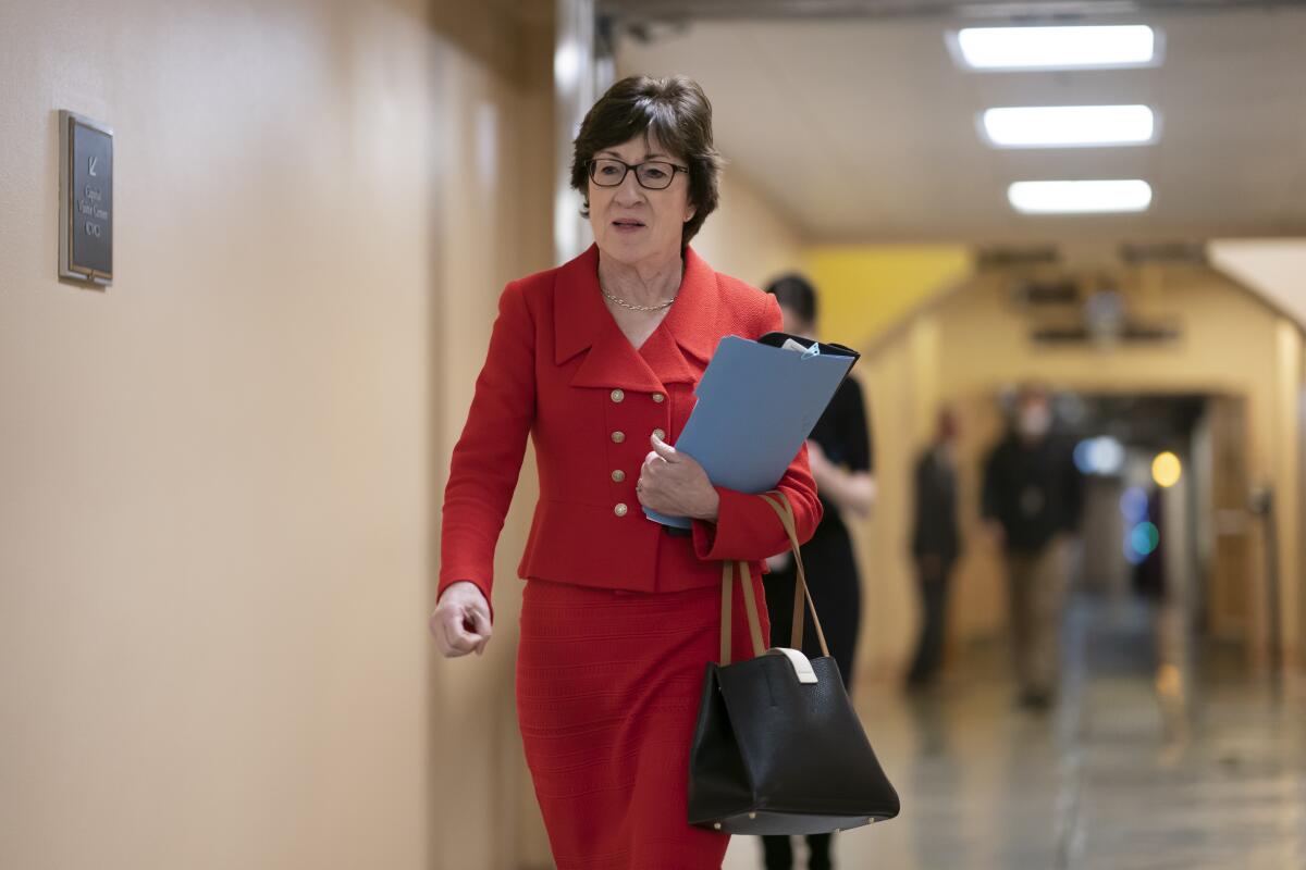 Sen. Susan Collins wears a red suit while walking down a hallway