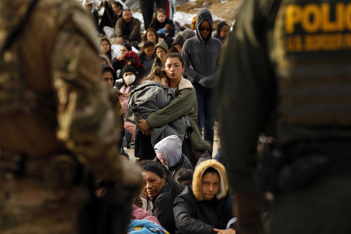 A group of seated people is seen between two standing Border Patrol agents