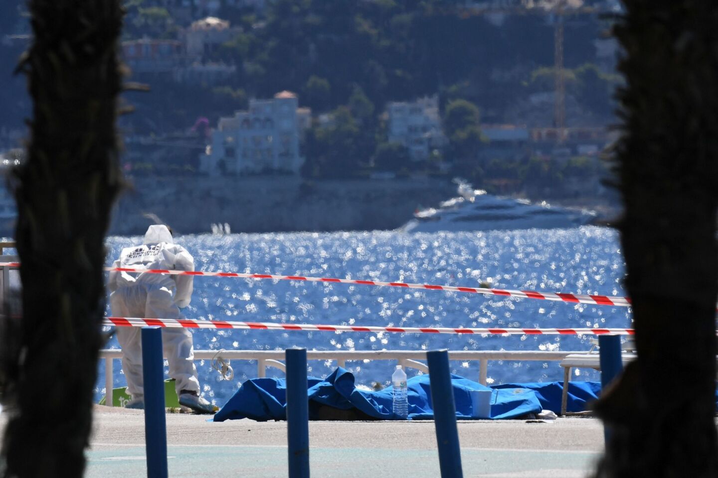 A forensic expert examines dead bodies covered with a blue sheet on the Promenade des Anglais seafront in Nice, a day after a gunman smashed a truck into a crowd of revellers celebrating Bastille Day.