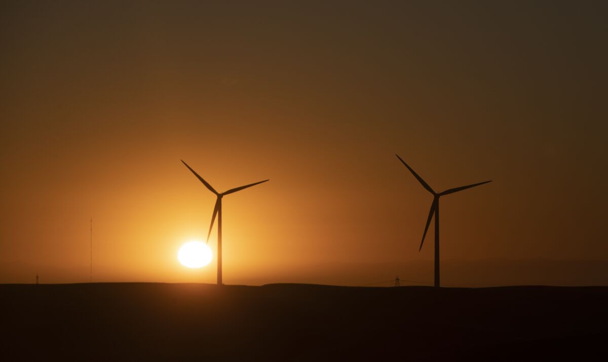 The sun rises behind wind turbines