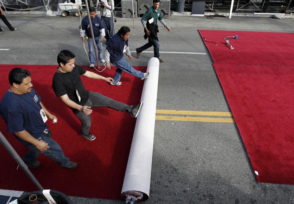Workers roll out a red carpet along a street