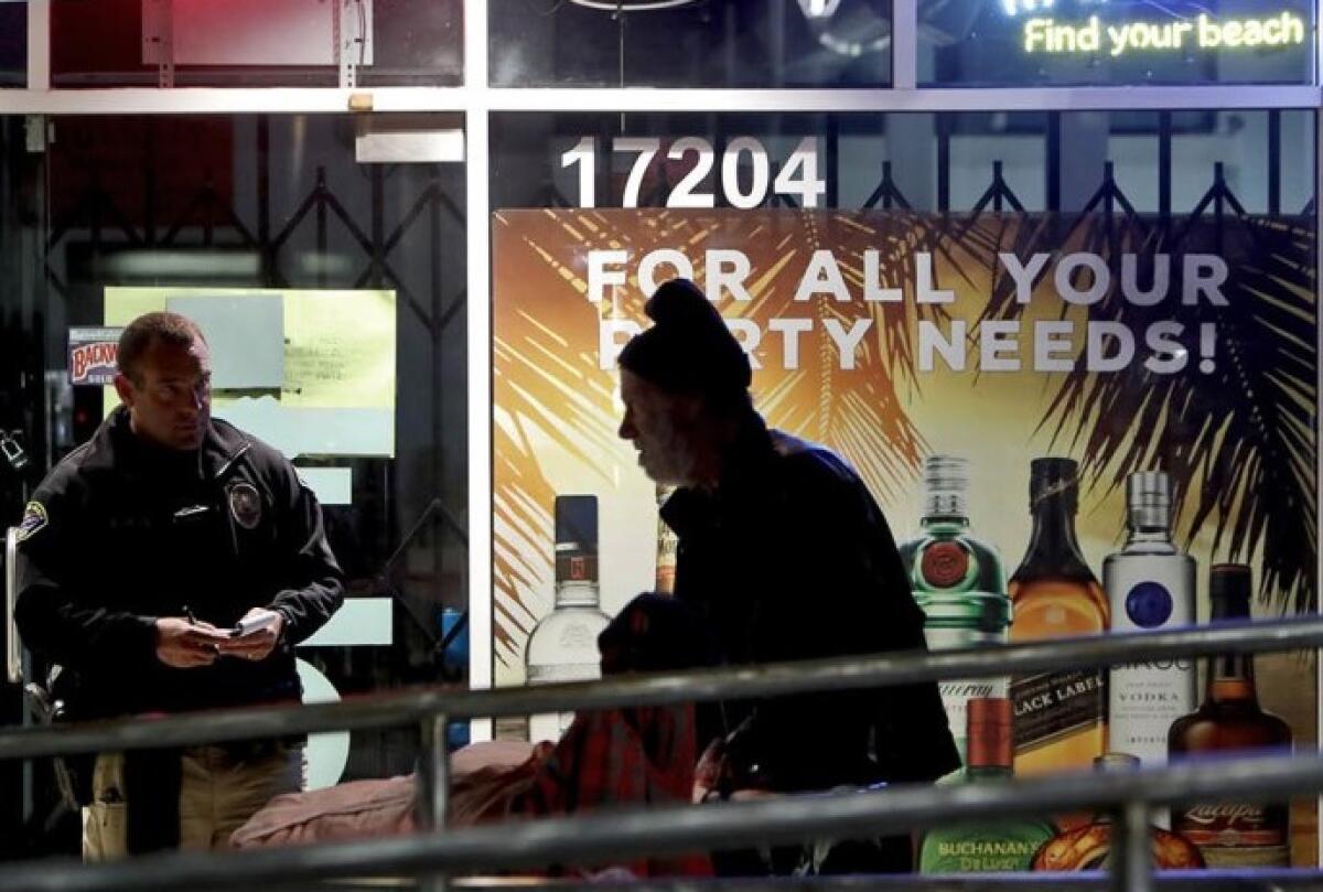 Huntington Beach Homeless Task Force officer Jed Dineen speaks with a homeless man who was sleeping outside a liquor store at Warner Avenue and Pacific Coast Highway on Feb. 13.