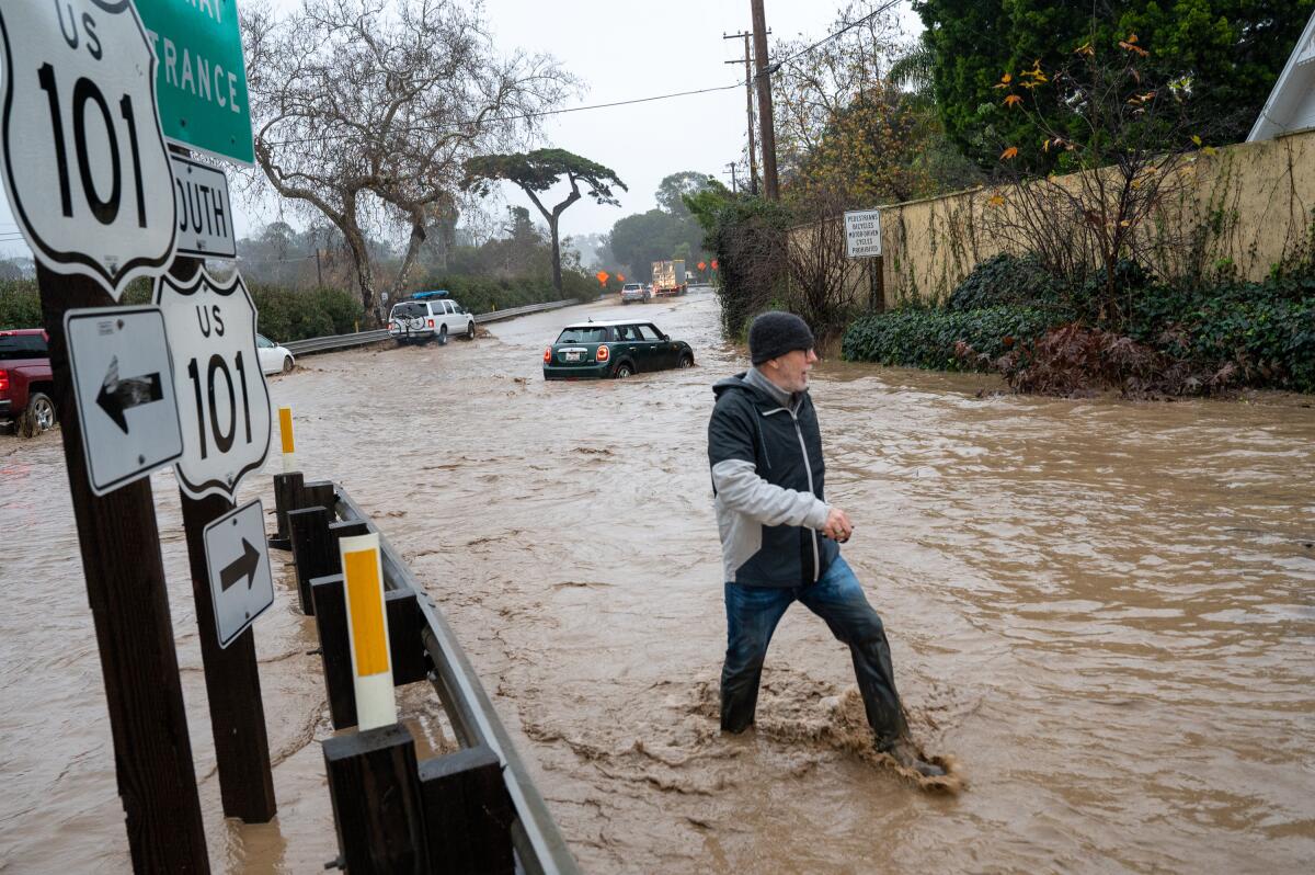 A man walks through a flooded road away from his stalled car.