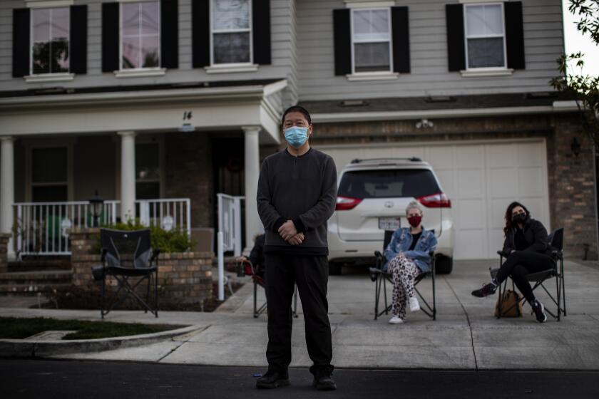 MISSION VIEJO, CA - FEBRUARY 25, 2021: Haijun Si stands in front of his Ladera Ranch family home as neighbors gather in front to form a nightly security detail after local teens have harassed the family by throwing rocks and yelling racial slurs on February 25, 2021 in Mission Viejo, California.(Gina Ferazzi / Los Angeles Times)