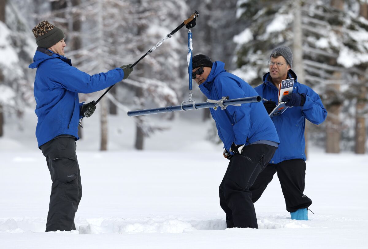 Three men in blue parkas use tubes to measure snowpack.