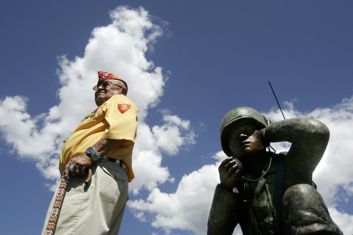 Navajo code talker Samuel Sandoval stands next to a statue of a soldier holding a communication device.