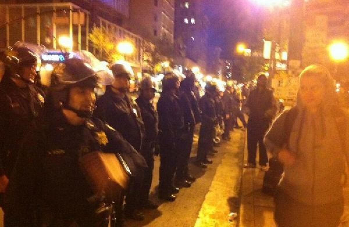 Officers respond to a tense protest in Oakland by forming a line with visors on, pushing protesters away from curb.