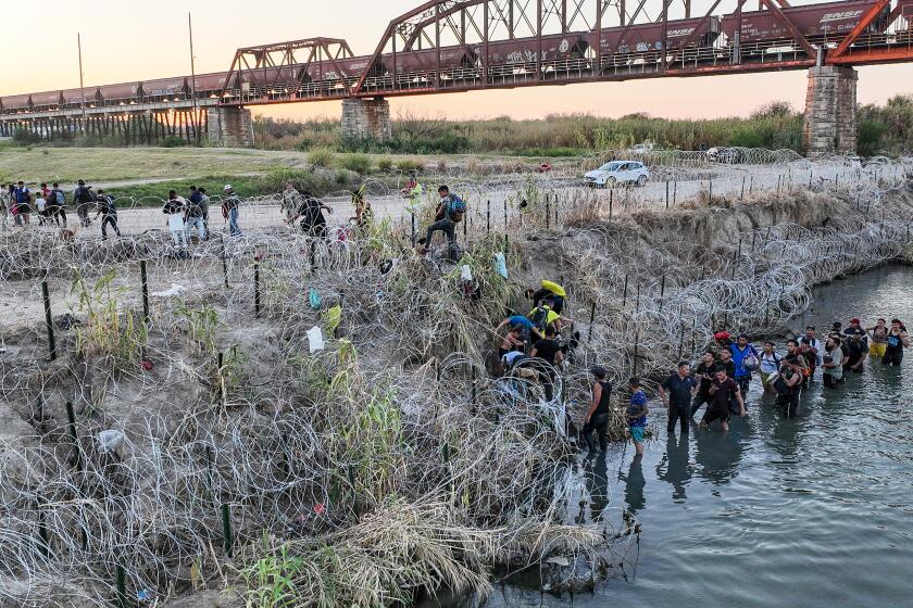 Eagle Pass, Texas, Saturday, September 23, 2023 - People who crossed the U.S./Mexico border look for a passage way through razor wire on the Texas side of the Rio Grande. (Robert Gauthier/Los Angeles Times)