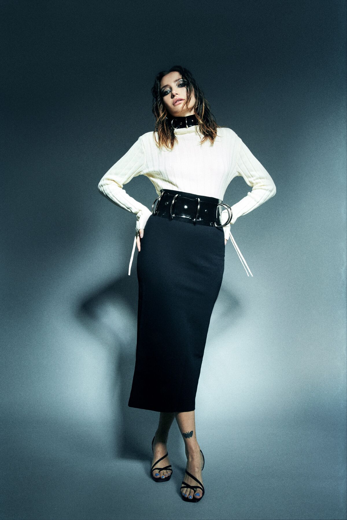 A model wears a black pencil skirt with a white long-sleeved top and a wide black belt and choker.
