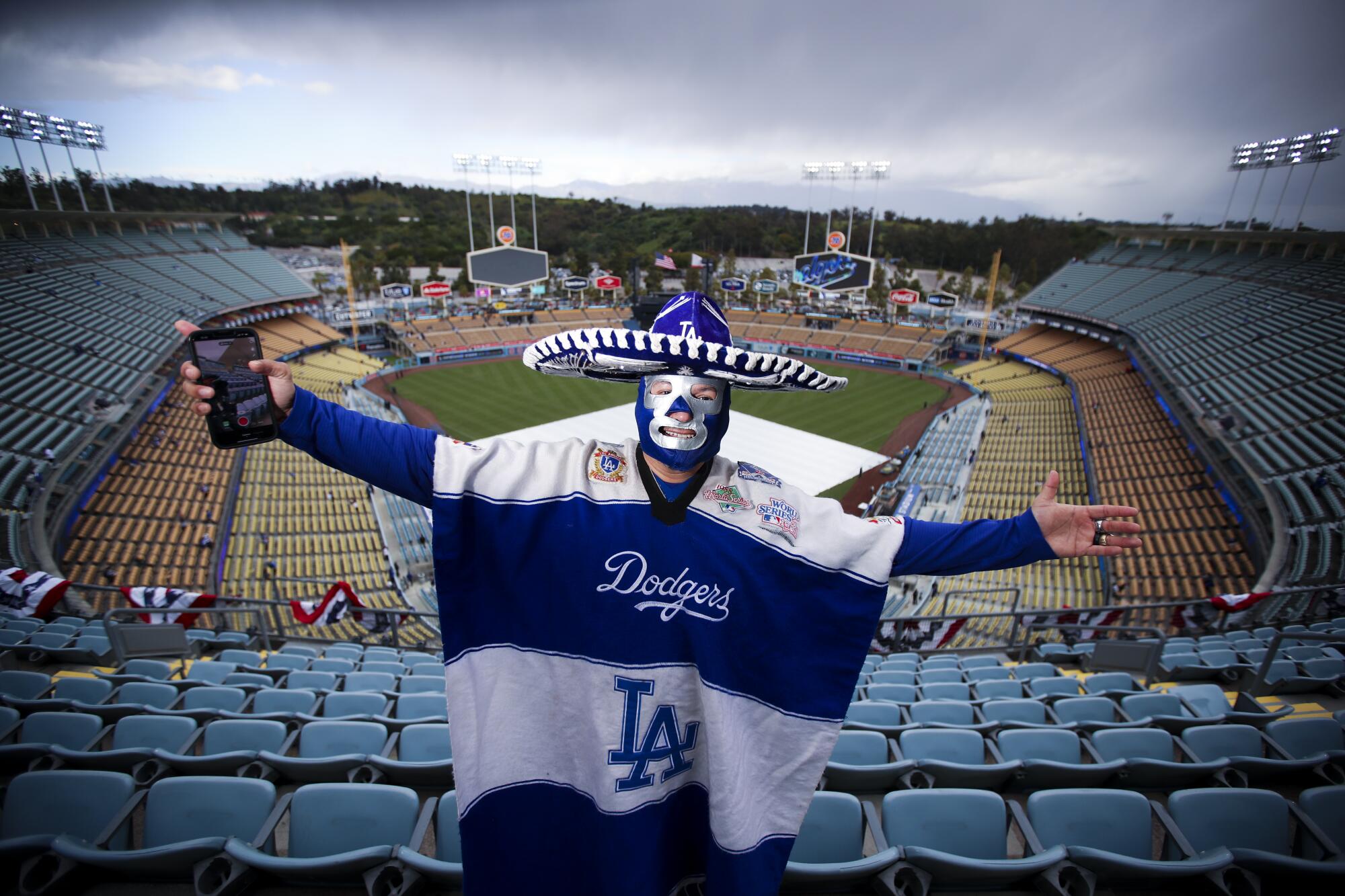  A man wearing a Dodgers serape, lucha libre mask and sombrero spreads his arms in the Dodger Stadium stands