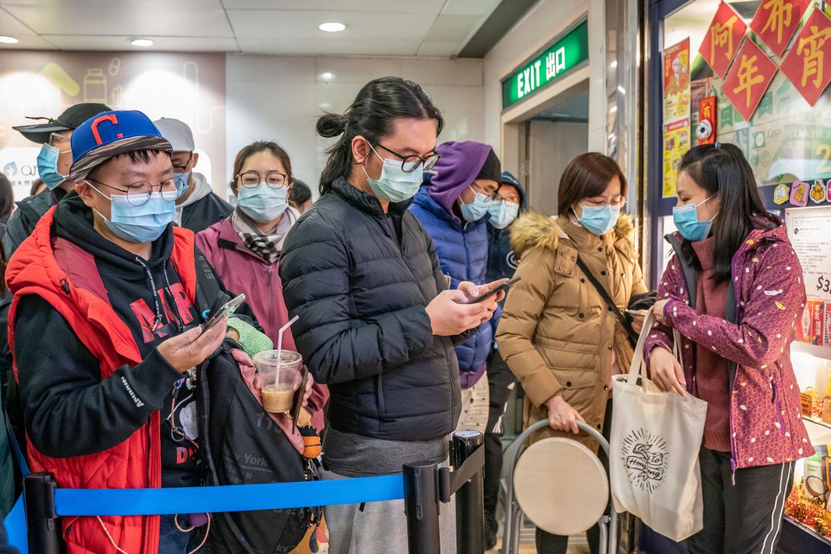 People in surgical masks wait in line at a shopping mall in Hong Kong amid the spread of the COVID-19 coronavirus.