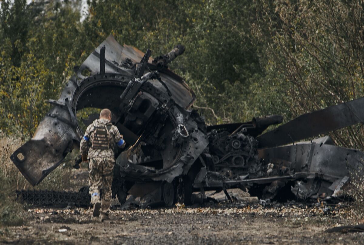 A Ukrainian soldier passes by a Russian tank damaged in a battle 