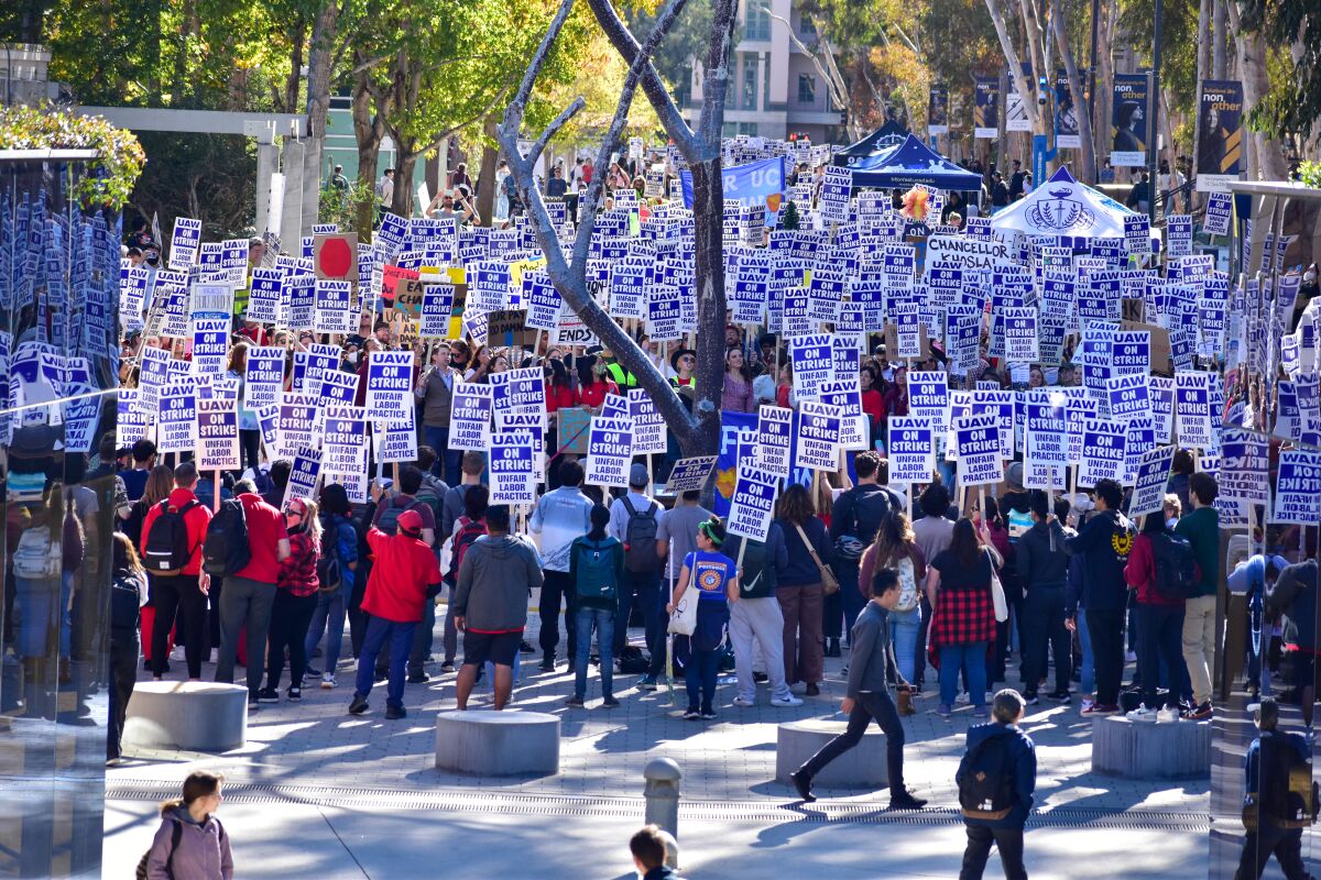 A large crowd of people hold up matching signs during a labor strike outdoors.