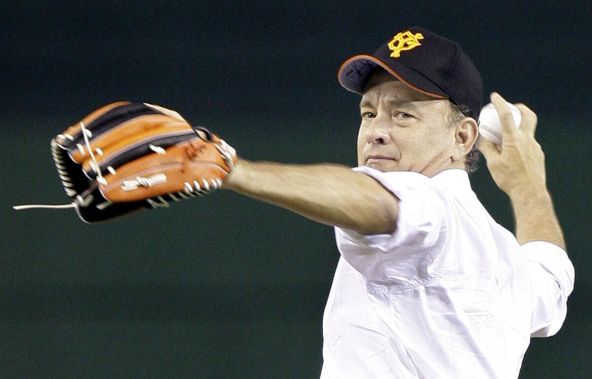 Tom Hanks is wearing a baseball cap while throwing the first pitch before the start of a Japanese professional baseball game.