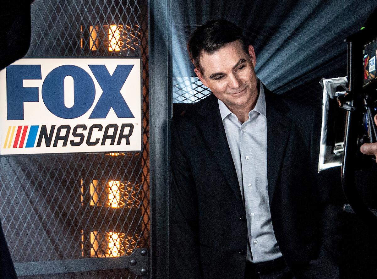 Former NASCAR driver Jeff Gordon stands next to a Fox Sports NASCAR sign.