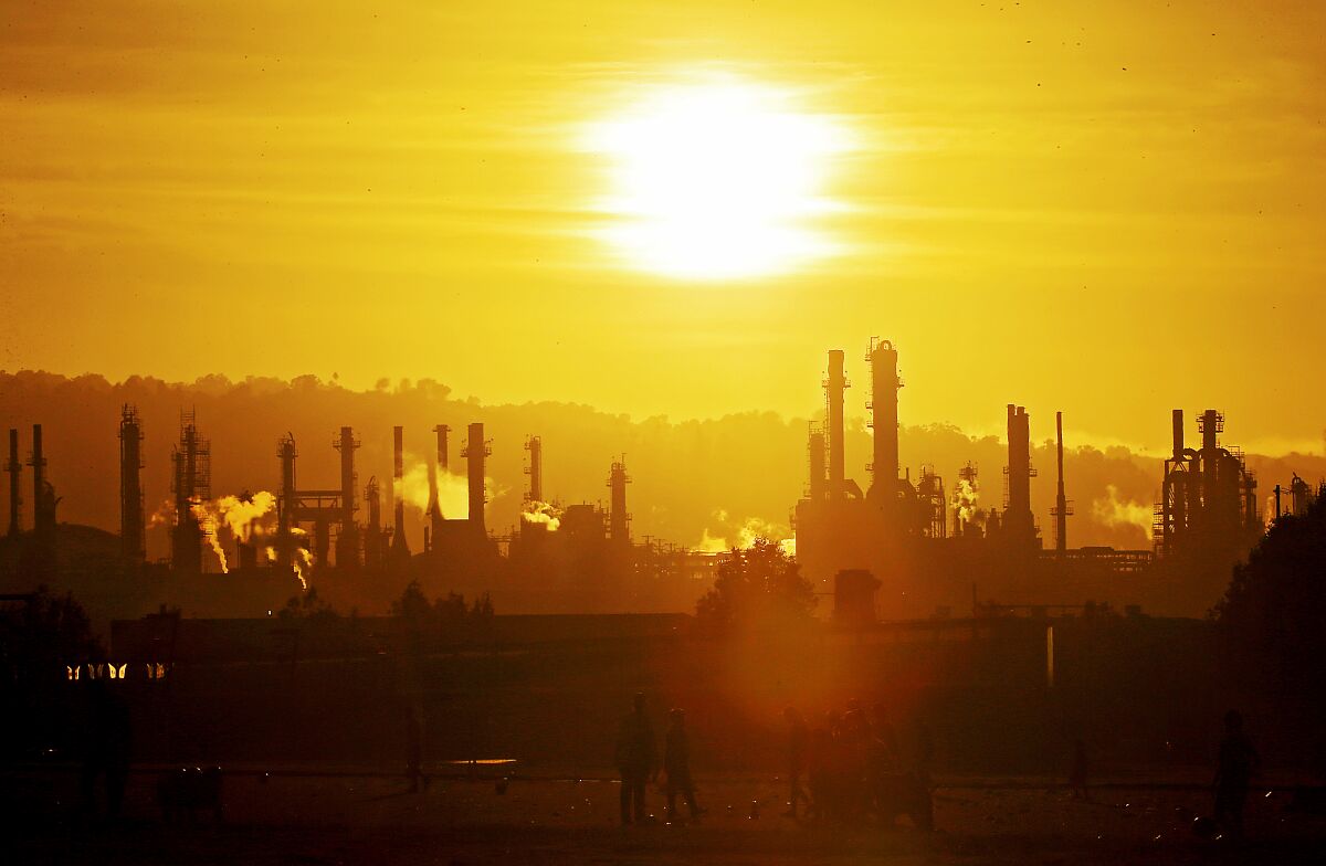 Smokestacks from a refinery silhouetted by a sunset