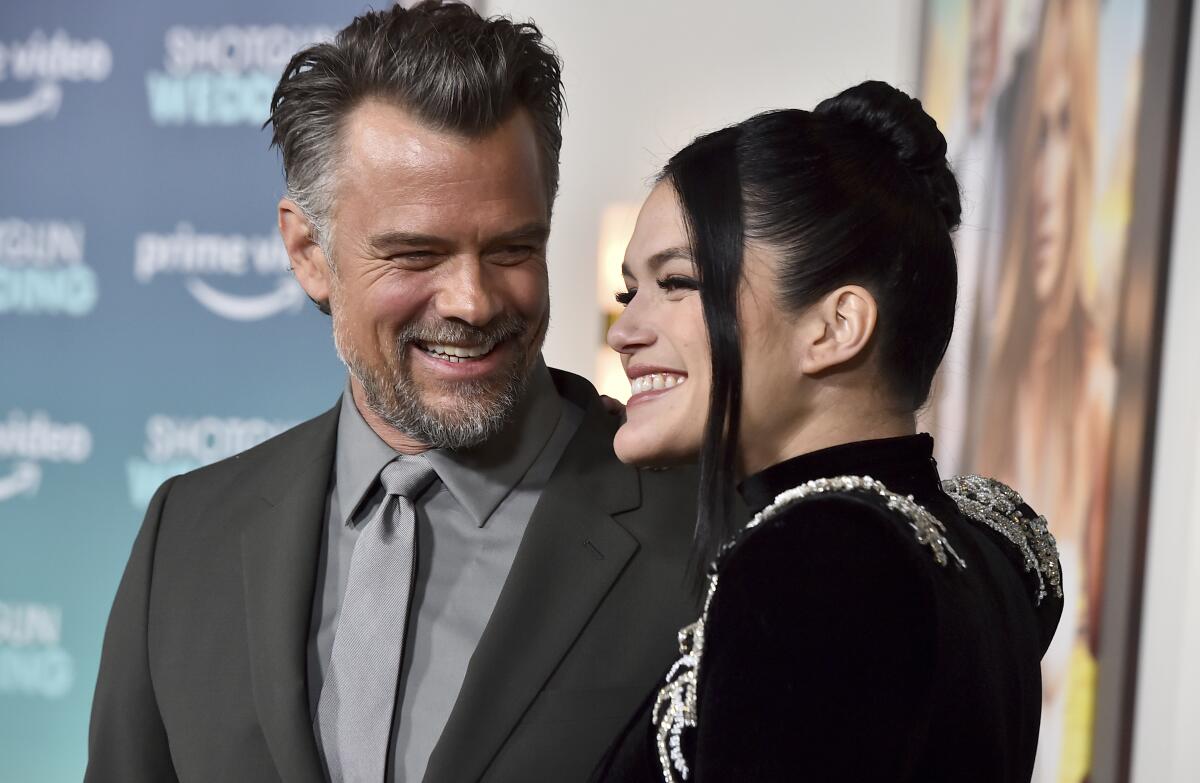 A man in suit and tie and a woman in a black jacket stand together, smiling.