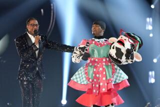 Nick Cannon in a sparkly black suit standing next to Ne-Yo dressed in a pink and turquoise dress, holding a fake cow head