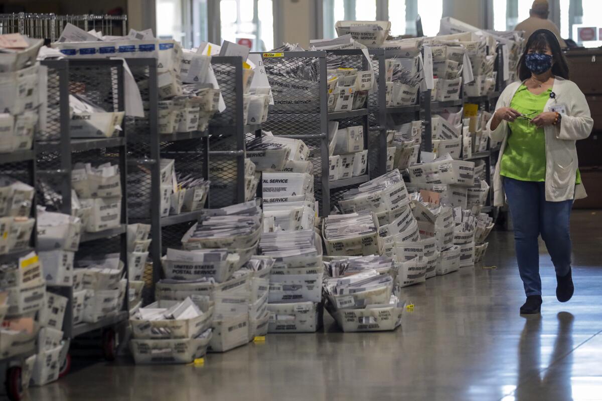 A woman walks by piles of ballots at a Los Angeles County Registrar of Voters' satellite office in Pomona in 2021.
