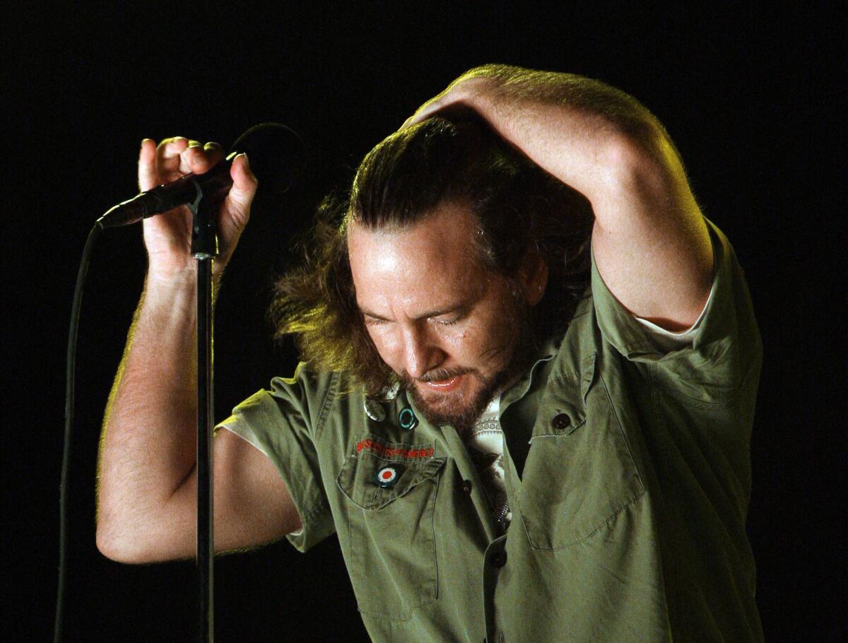 Pearl Jam's Eddie Vedder hanging from a microphone stand while tilting his head forward and brushing his hair back with one hand.