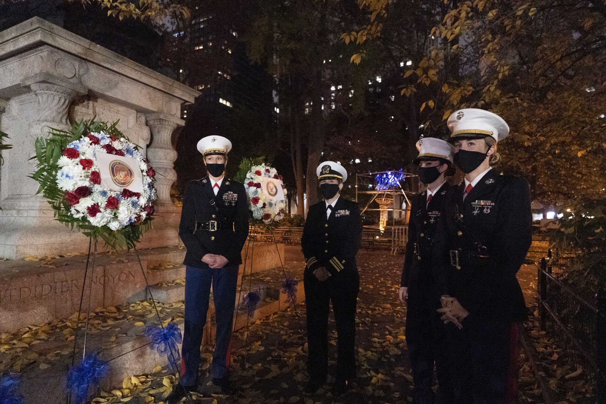 Women in an honor guard stand before wreaths at the Eternal Light Flagstaff in Madison Square Park in New York.