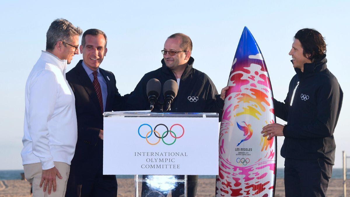 Patrick Baumann, center, and Christophe Dubi, right, of an International Olympic Committee delegation are given a surfboard by LA 2024 Chairman Casey Wasserman, left, and L.A. Mayor Eric Garcetti at Santa Monica Beach.