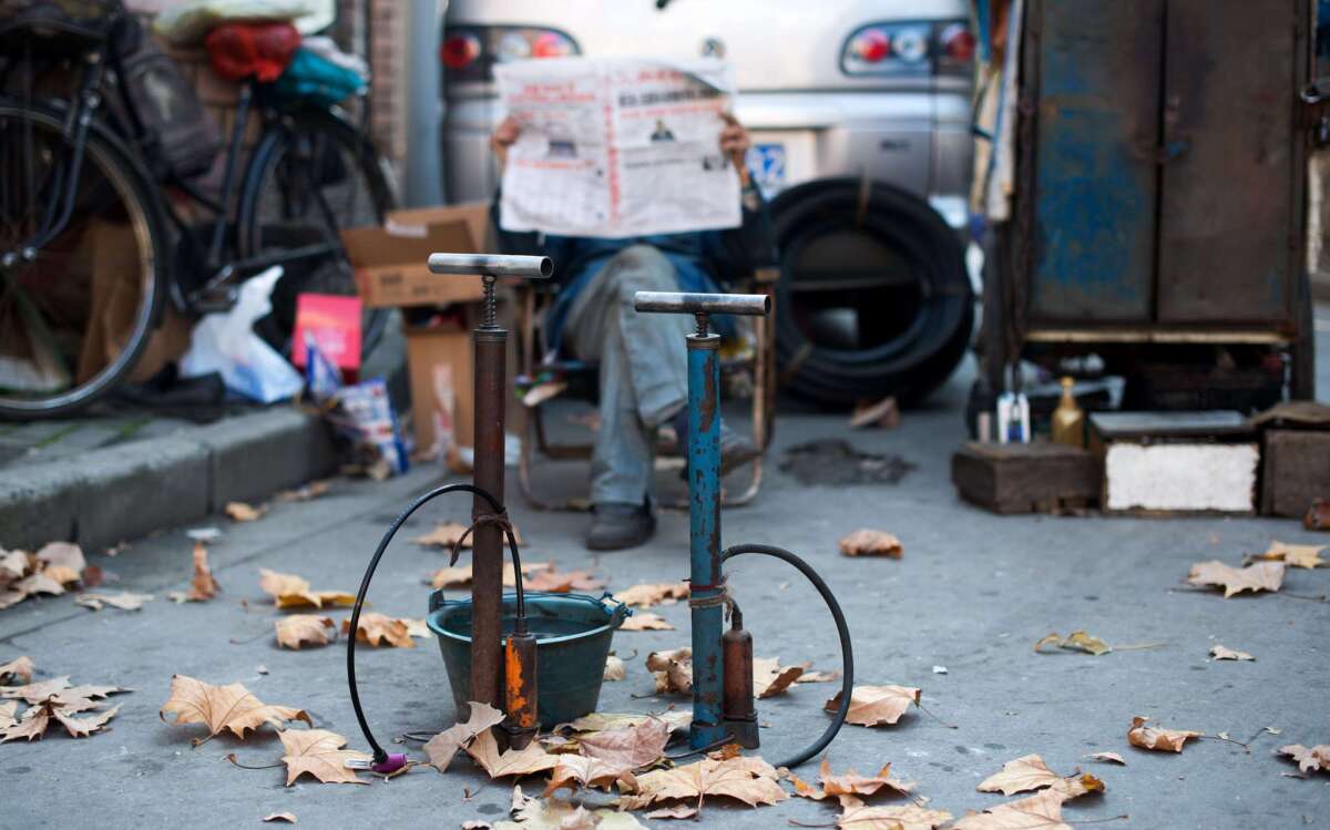 A man who repairs bike tires reads a newspaper behind his air pumps in Shanghai on Nov. 27, 2014. China's media regulator has issued an order restricting puns and wordplay in copy.