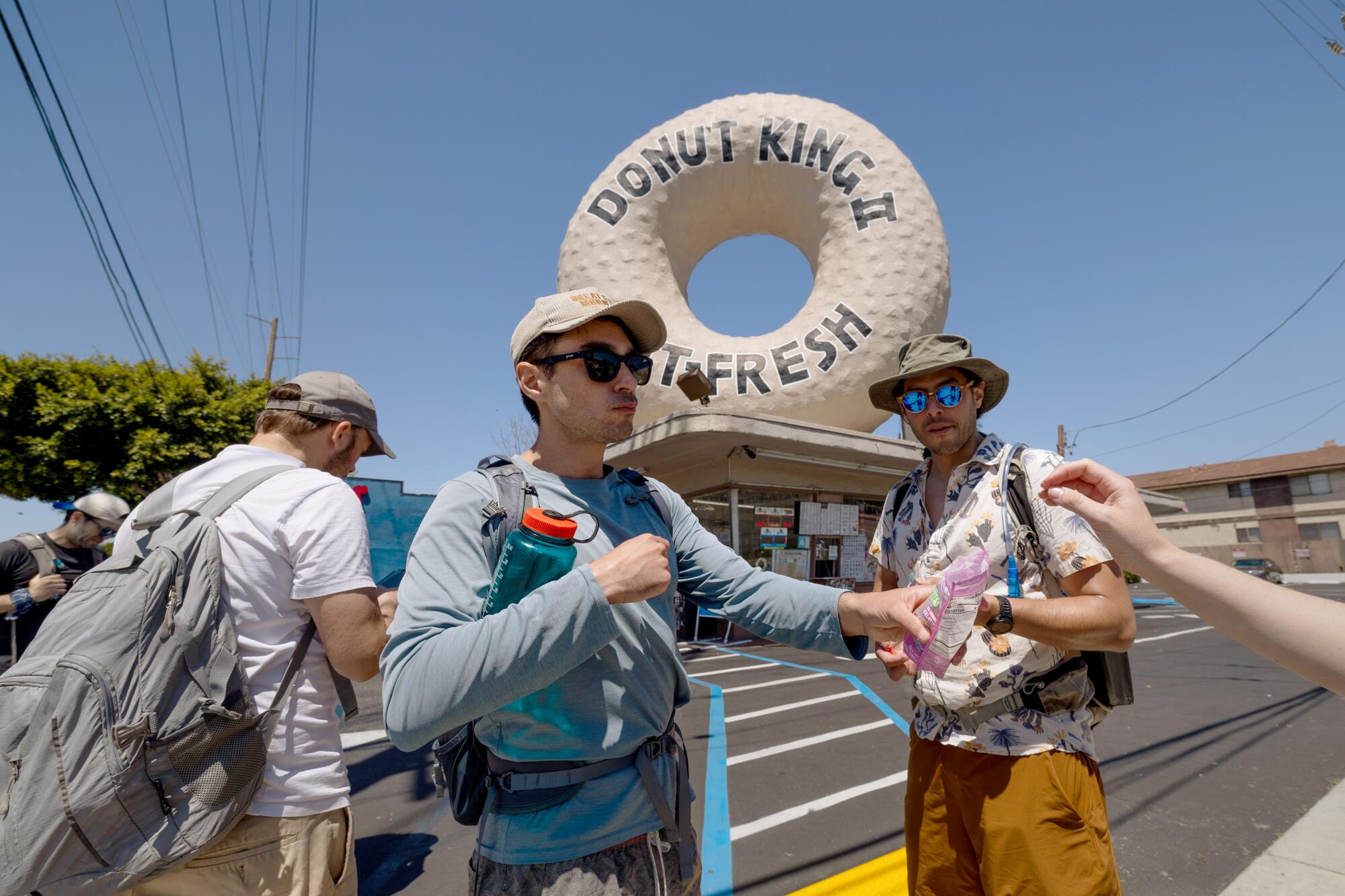 Un hombre rodeado de amigos sostiene una bolsa abierta de bocadillos frente a un Donut King.