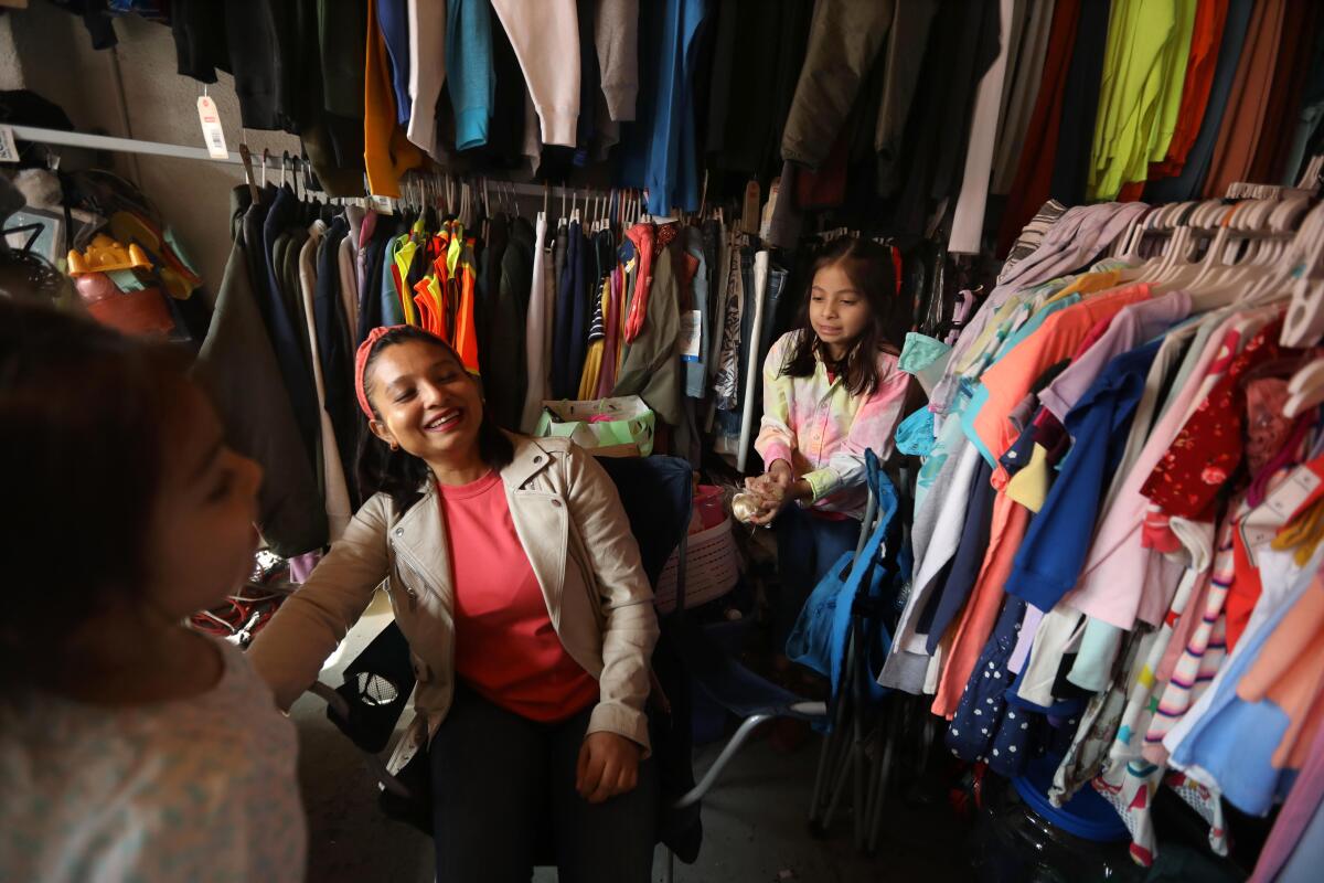A woman and two children amid clothes racks in a store.
