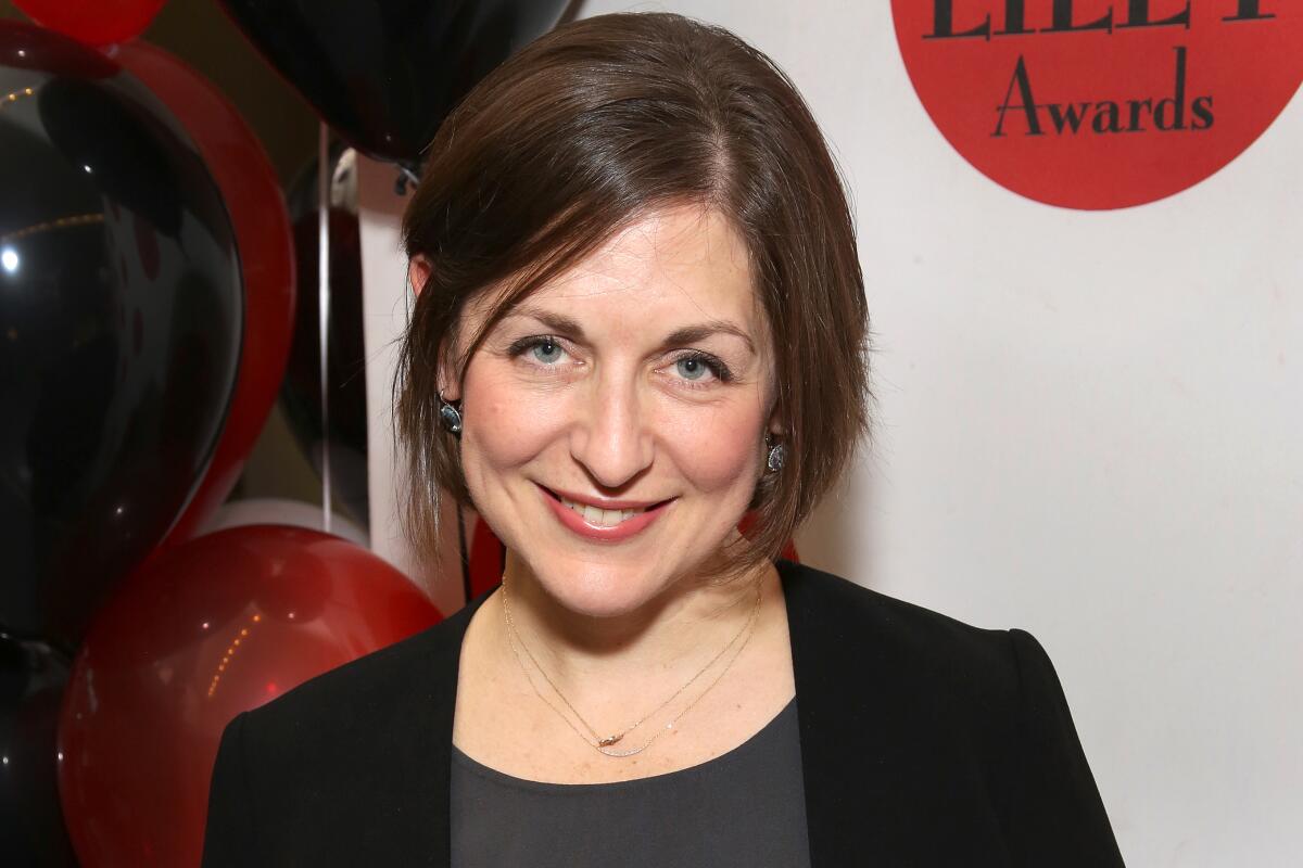 A woman smiling, wearing a gray shirt and a black blazer.