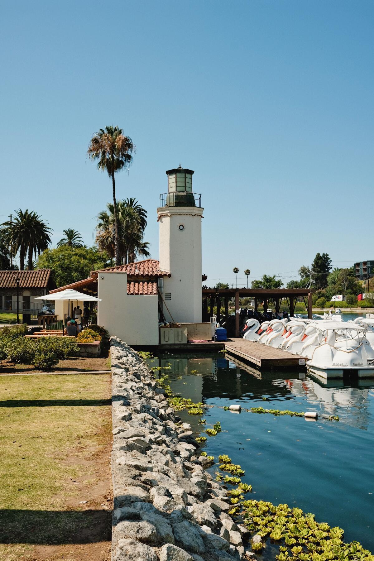 A vertical side exterior of Piknik cafe along an edge of Echo Park Lake. The famous swan boats at a dock at right.