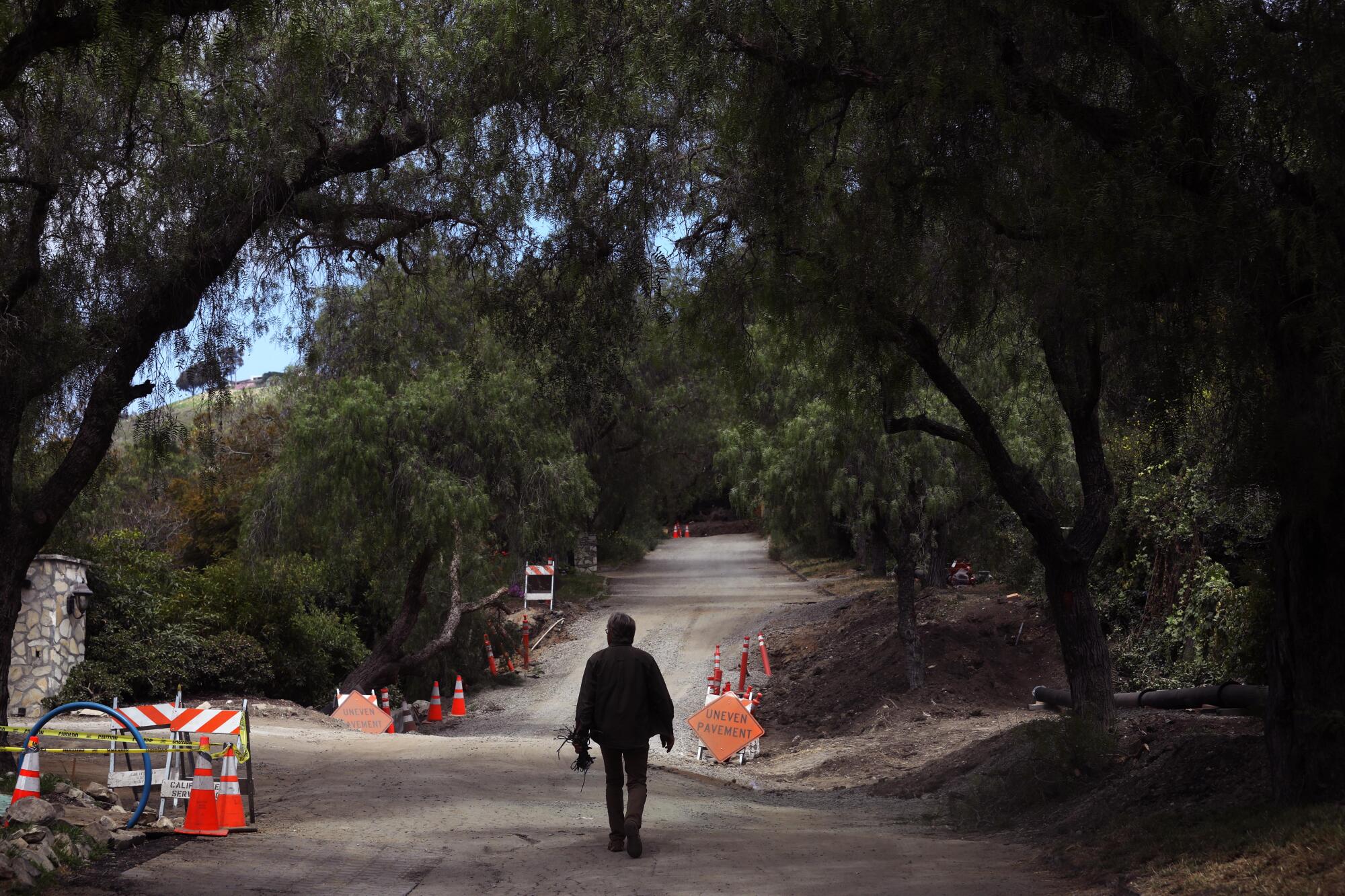 A man walks on an uneven street marked by warning signs.