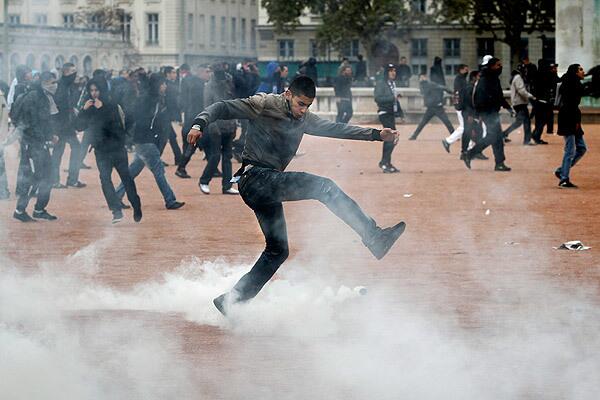 A youth kicks a tear gas grenade during clashes with authorities. Some airliners steered clear of France, drivers searched for gasoline and police clashed with increasingly violent youths amid a new round of nationwide strikes and protests over a bill raising the retirement age to 62.