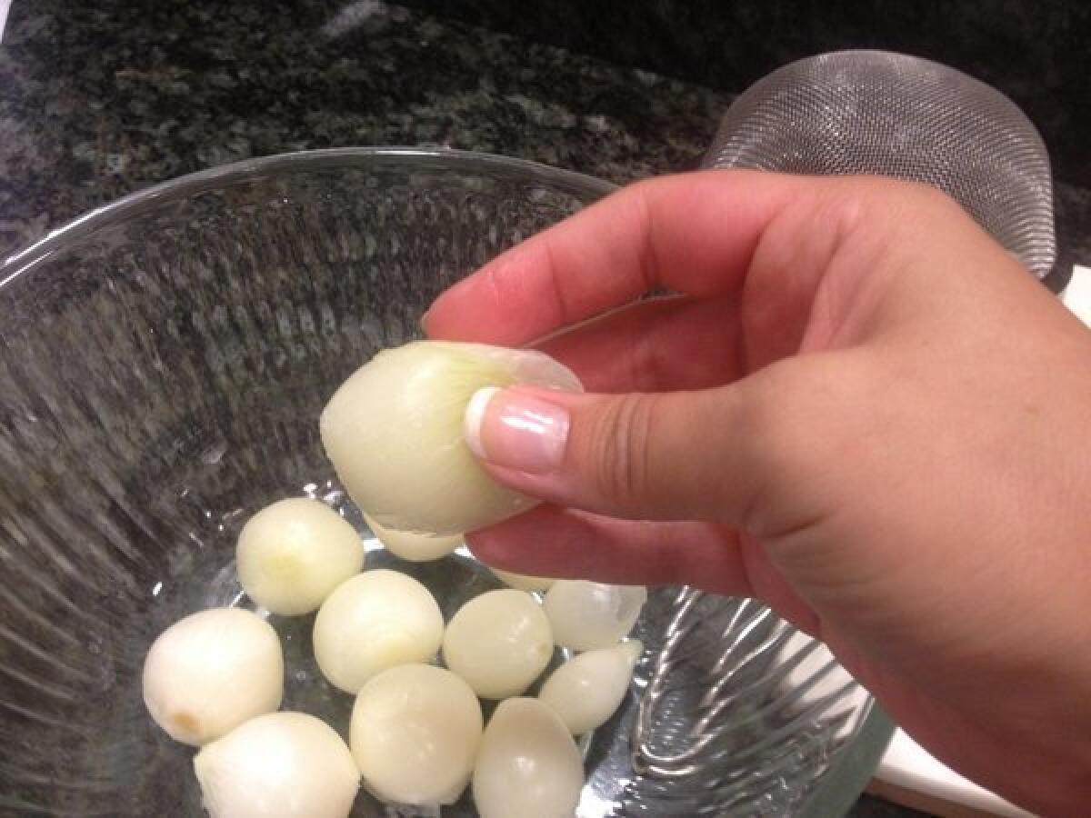 Pinch a blanched pearl onion to peel the outer layer.