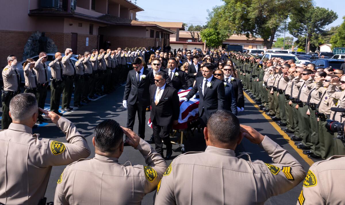 Sheriff's deputies in uniform line up and salute as pallbearers carry a casket outside a church