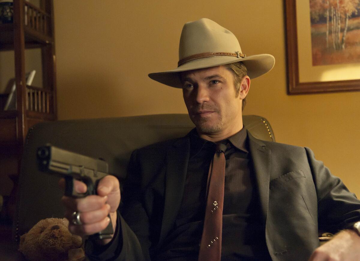 A man in a cowboy hat sitting in a chair and pointing a gun