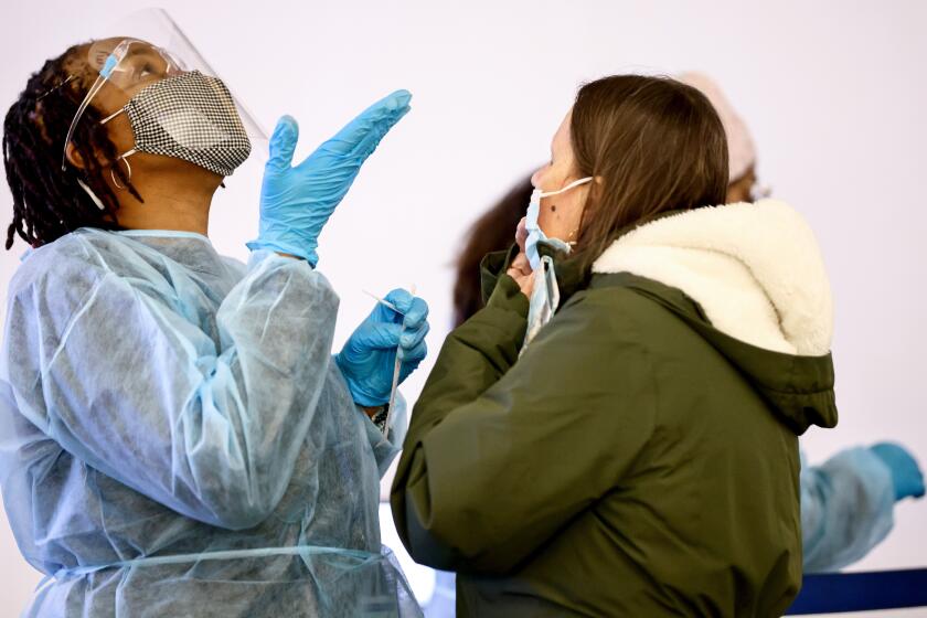 LOS ANGELES, CALIFORNIA - DECEMBER 21: Merline Jimenez (L) provides direction before administering a COVID-19 nasopharyngeal swab to a person at a testing site located in the international terminal at Los Angeles International Airport (LAX) amid a surge in Omicron variant cases on December 21, 2021 in Los Angeles, California. AAA estimates that over 109 million Americans will be traveling 50 miles or more during the holiday season between December 23 and January 2, an increase of 27.7% from 2020. (Photo by Mario Tama/Getty Images)