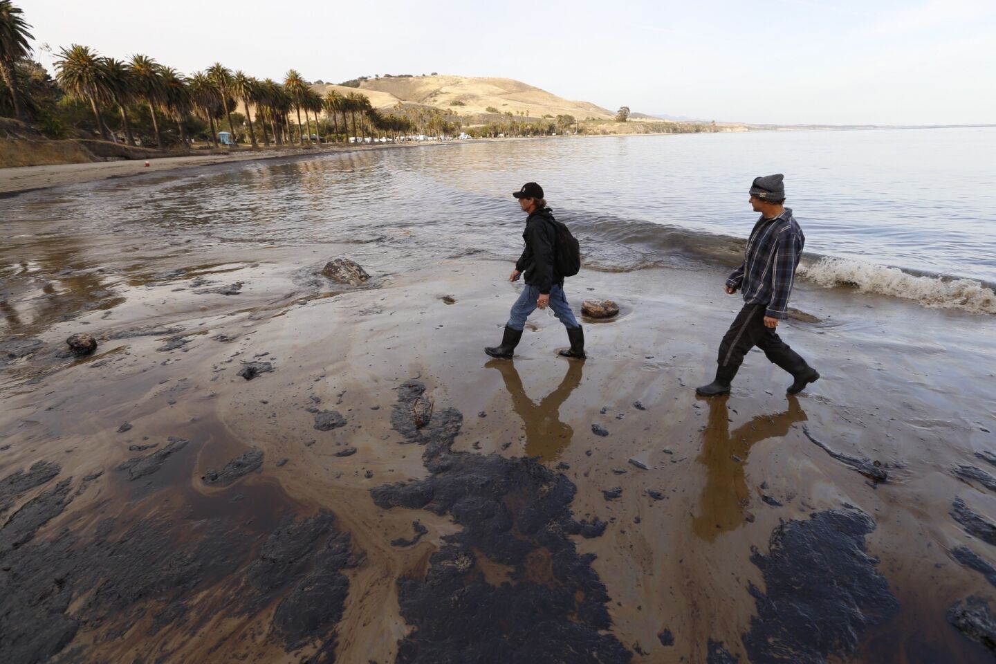 Morgan Miller, left, and Josh Marsh walk the oil-coated shore at Refugio State Beach.