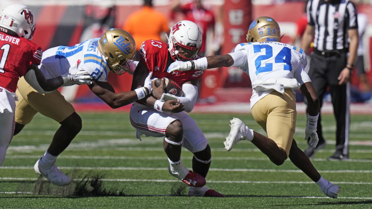 Utah quarterback Nate Johnson, center, carries the ball as he is tackled by UCLA's JonJon Vaughns and Jaylin Davies.
