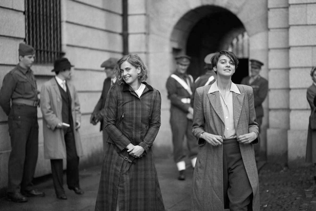 In a black-and-white film still, two women in coats smile