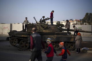 Children stand atop a tank as a man walks by with two children, holding hands