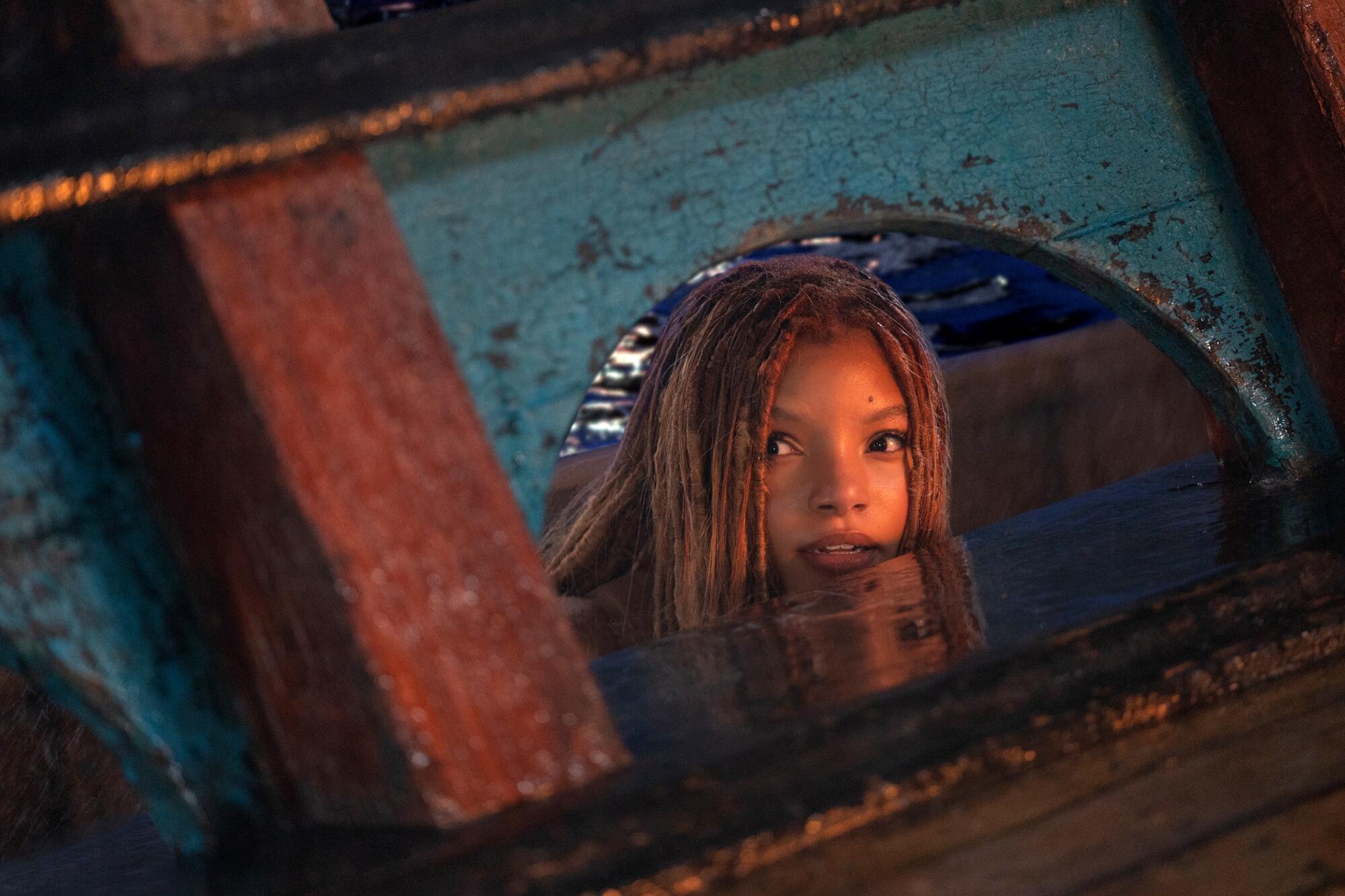 A mermaid pokes her head out of the water beside a ship.