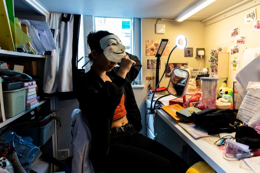 April Lui holds a mask she uses to hide her identity when she attends a protest, as she sits for a portrait in her bedroom at home in Lai Chi Kok, Hong Kong on November 16th, 2019. April is reluctant to migrate to Canada but has been given no choice in the matter by her mother, Virginia, who wants to ensure the safety of her daughter. Photo by Suzanne Lee / PANOS for The L.A. Times