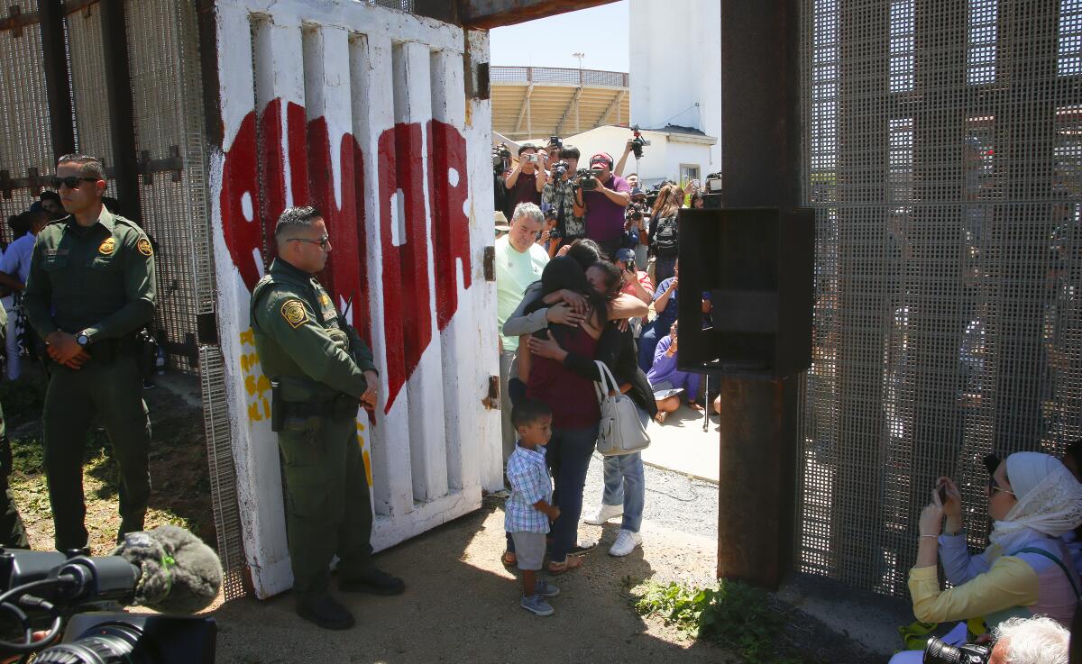 Family members hug in an open doorway in the border wall as officers watch.