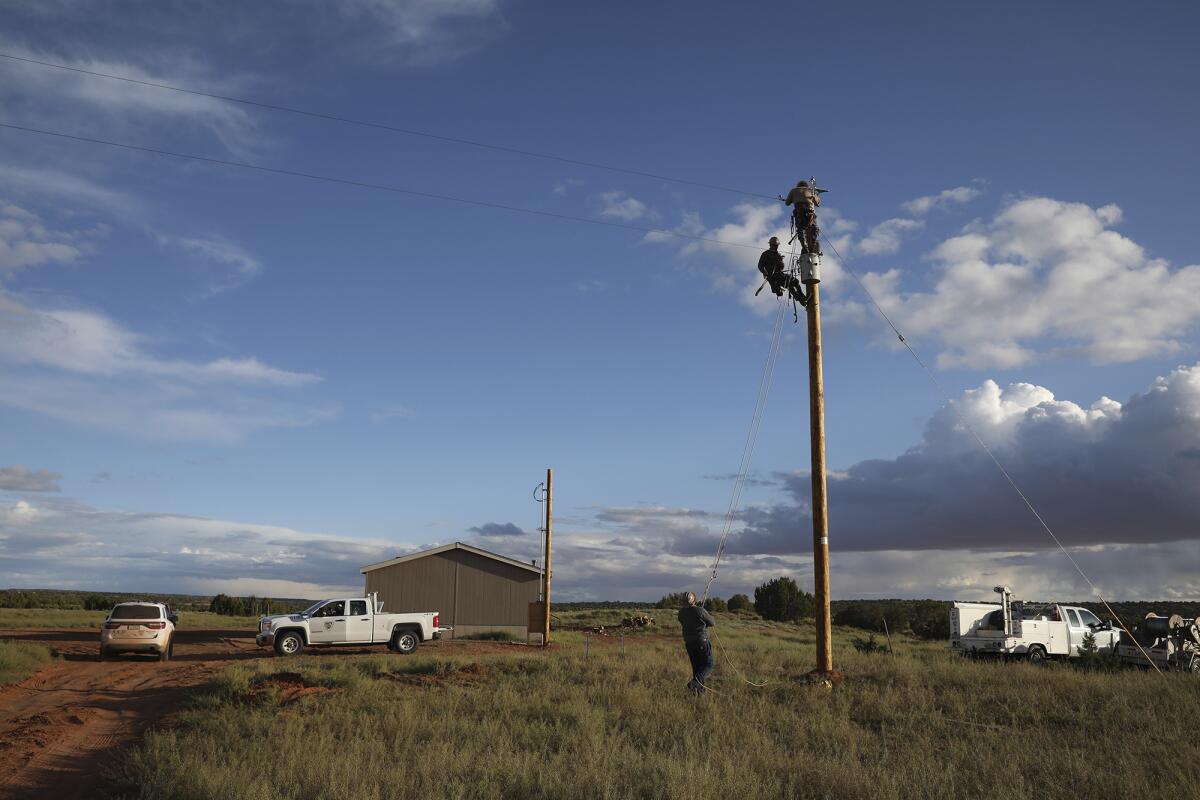 Two people perch atop a power pole on a remote plain, with one onlooker