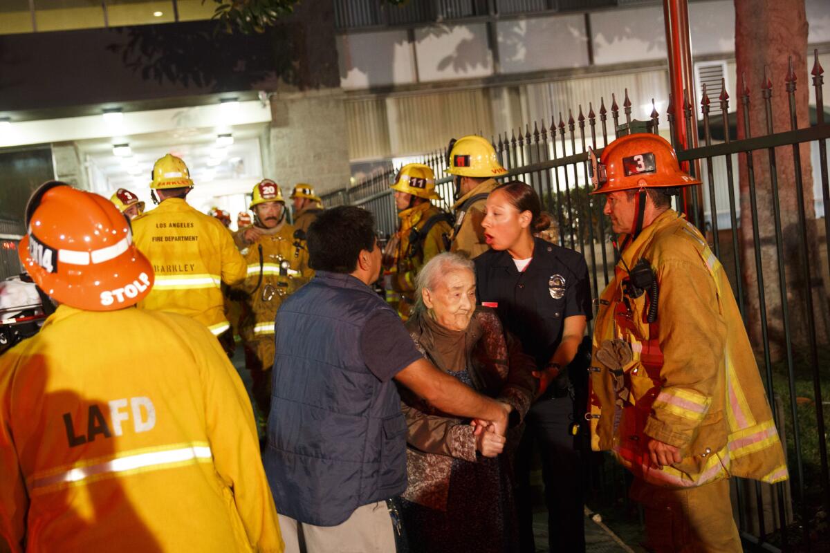 Firefighters help a woman evacuate from a 15-story high-rise apartment complex that erupted in fire Monday evening.